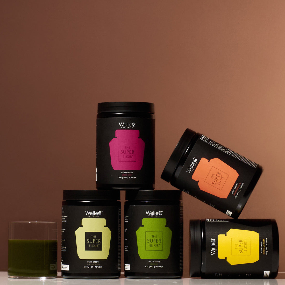 Five jars of health supplements stacked with a glass of green drink.