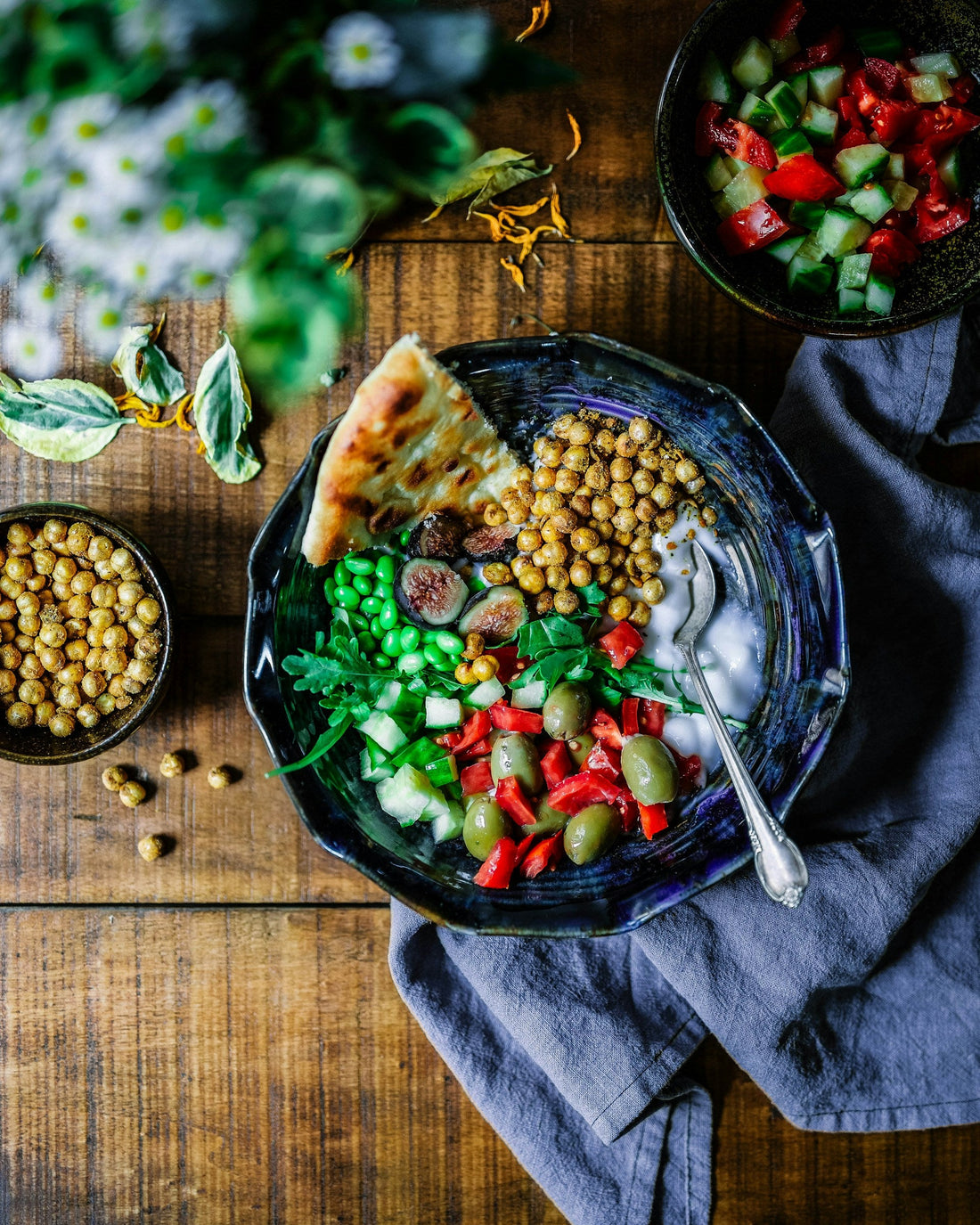 A colorful bowl of salad with pita bread and chickpeas on a wooden table.